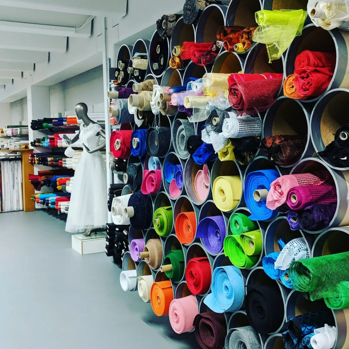 Wand aus Röhren mit aufgerollten Stoffen in allen Farben bei Hager Stoffe
